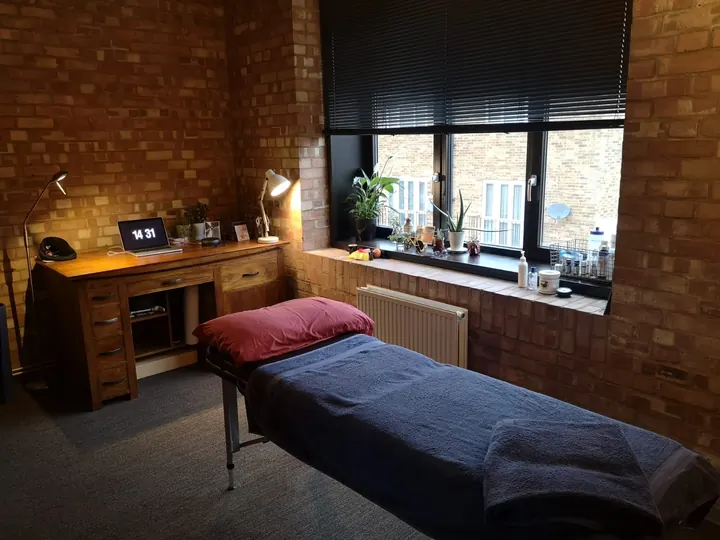 The Sharp Movement treatment room: massage table, desk and big windows in a brick-walled studio